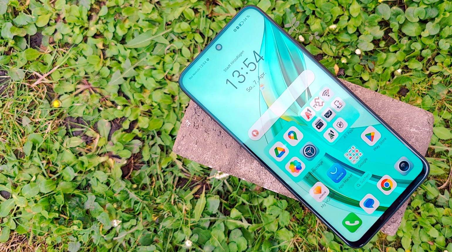 Honor 90 Smartphone auf Ziegel mit grüner Blumenwiese im Hintergrund