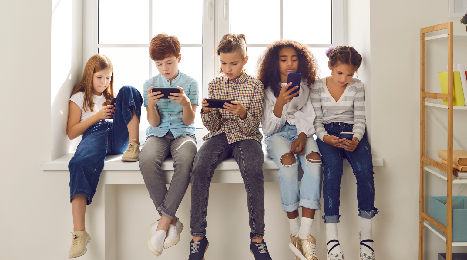 Fünf Kinder sitzen zusammen auf einer Fensterbank mit Smartphones.