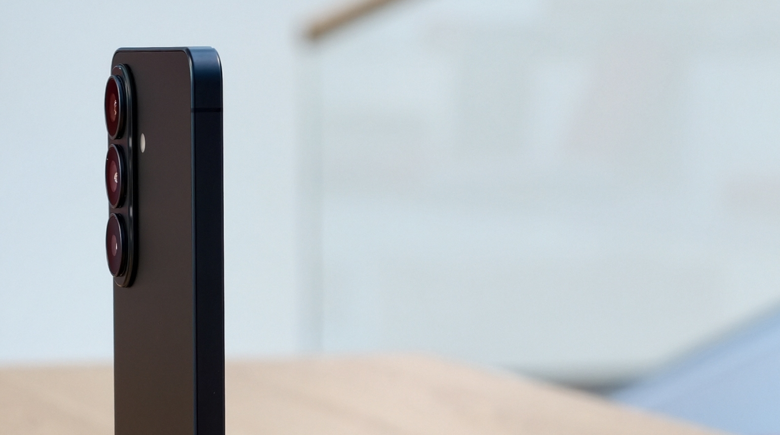 Smartphone mit drei herausstehenden Kameralinsen im Profil auf einem Holzti