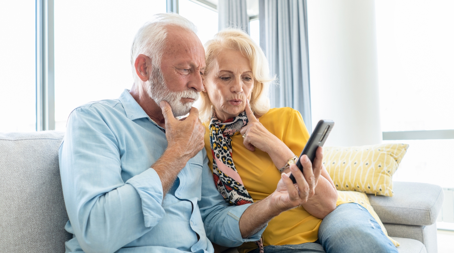 Älteres Paar sitzt auf dem Sofa und betrachtet gemeinsam ein Smartphone.