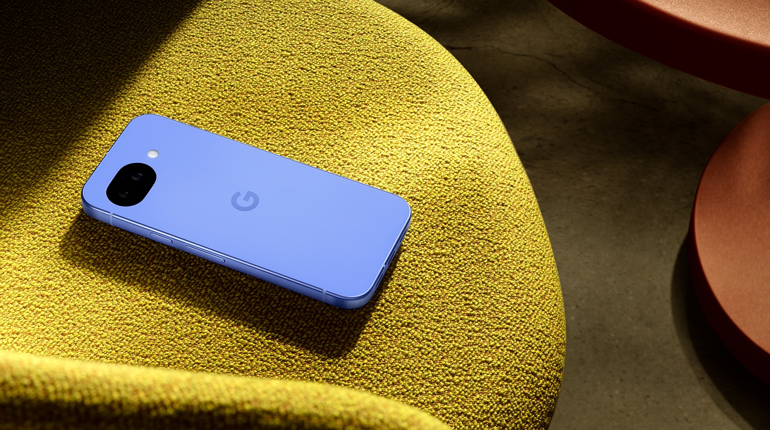 Blaues Google-Smartphone liegt auf einem gelben Stoffstuhl im Sonnenlicht