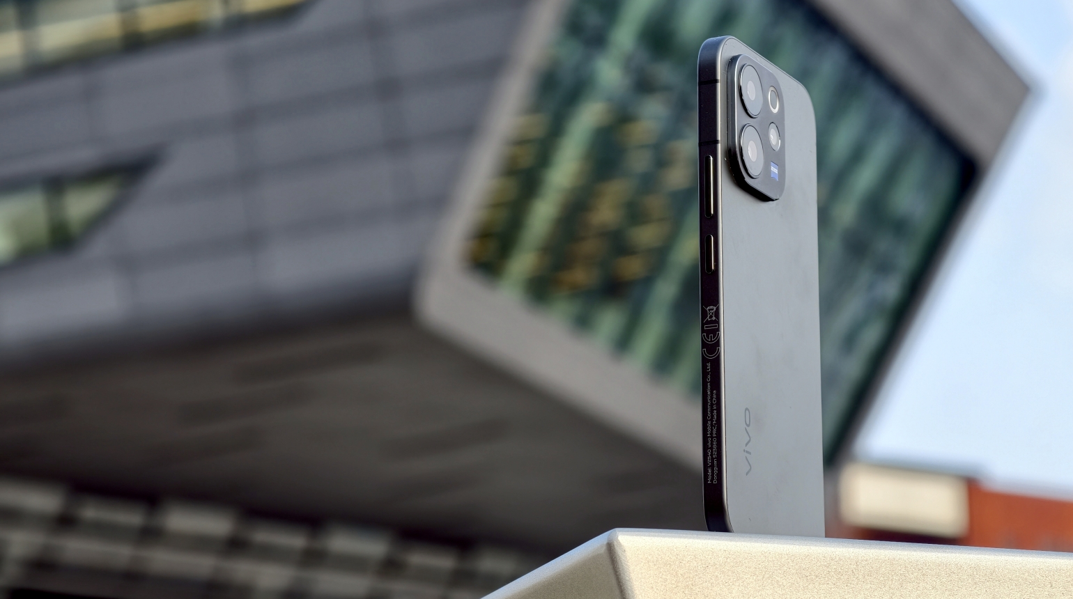 Smartphone der Marke Vivo mit drei Kameralinsen vor modernem Gebäude.
