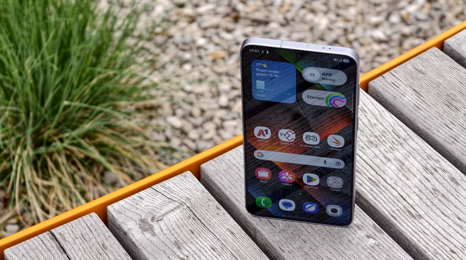 Smartphone steht auf einer Holzbank, Wetter-App zeigt und Regen, mehrere Ap