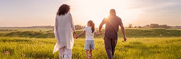 Eine Frau, ein Mann und ein Kind spazieren Hand in Hand auf einer grünen Wiese